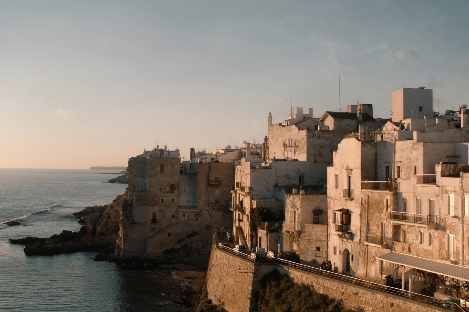 A whitewashed Puglian coastal town above the calm turquoise Adriatic at golden hour